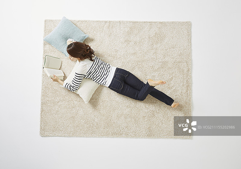 女人躺在地毯上看书的照片图片素材
