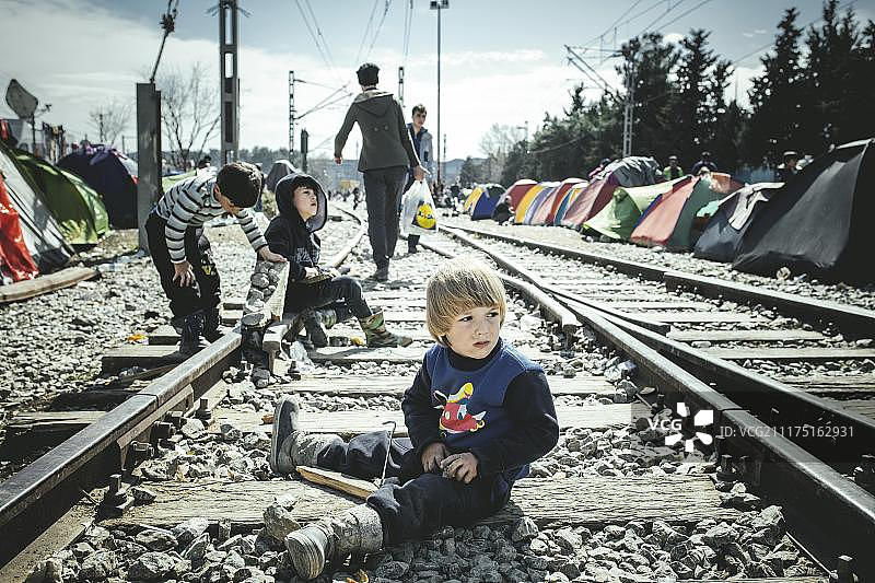 在希腊和马其顿边境的伊多梅尼难民营，一个小男孩坐在火车站的铁轨上图片素材