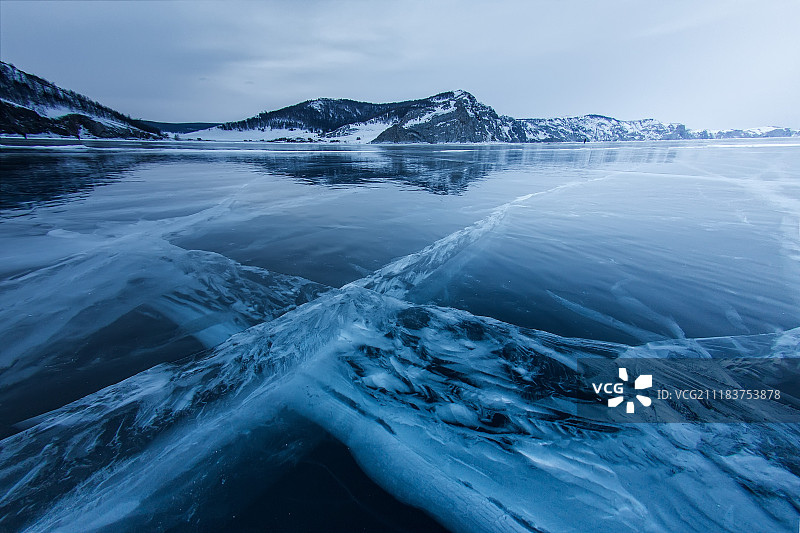 在落基山脉对面的贝加尔湖的厚冰上的深深的裂缝交叉图片素材