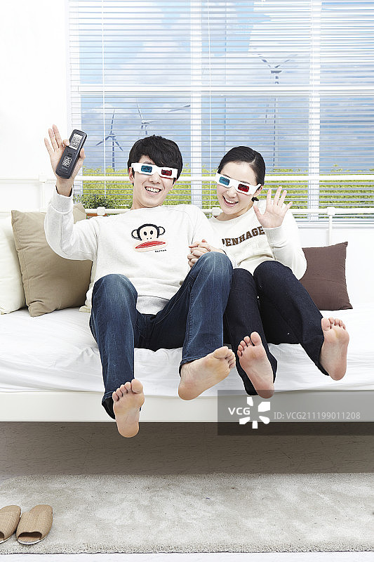 新婚夫妇戴3D眼镜坐在沙发上看电视的照片图片素材