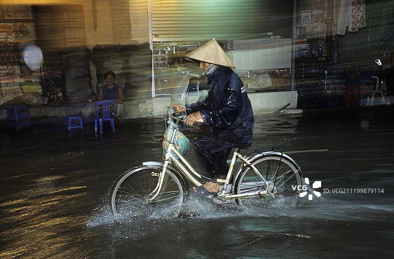 在越南的河内，人们骑着自行车，街道在大雨后被淹没，东南亚图片素材