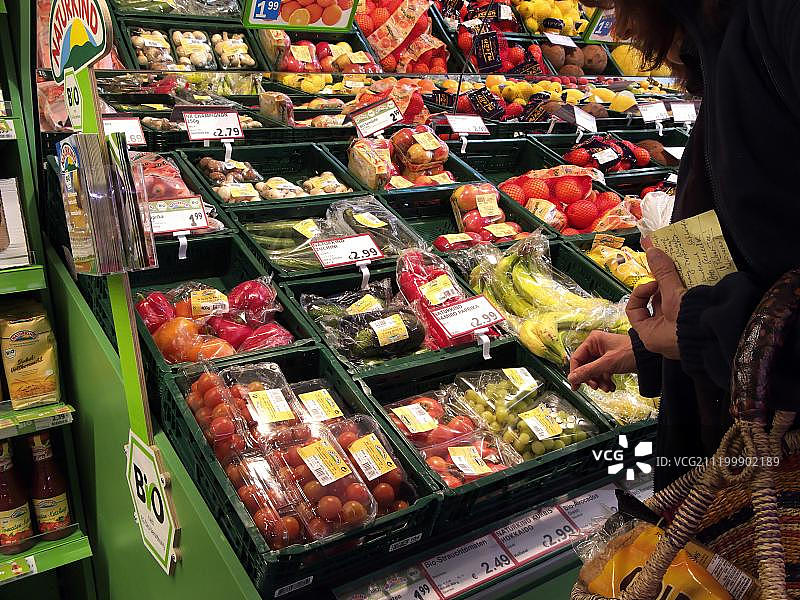 德国，欧洲，在超市里，购物者拿着购物清单看着有机水果和蔬菜的陈列图片素材