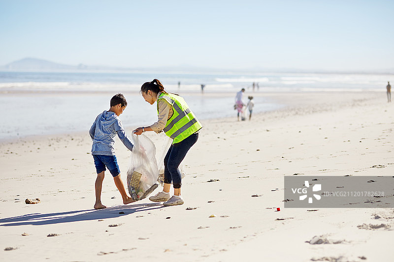 母亲和儿子在阳光明媚的沙滩上志愿者清理垃圾图片素材