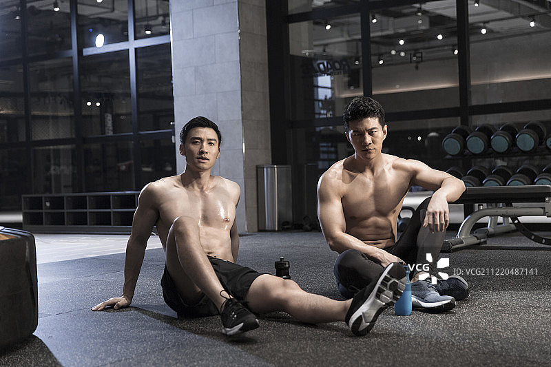 两个青年男子在健身房坐在地上休息图片素材