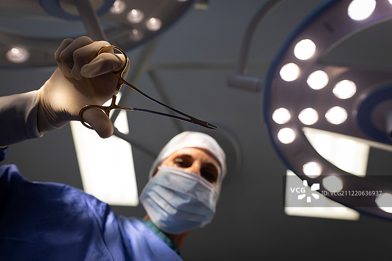 一个成熟的白种人女性外科医生在手术室中手持手术剪刀的低角度视图图片素材