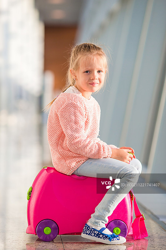 可爱的小女孩坐在机场的行李上等待登机图片素材