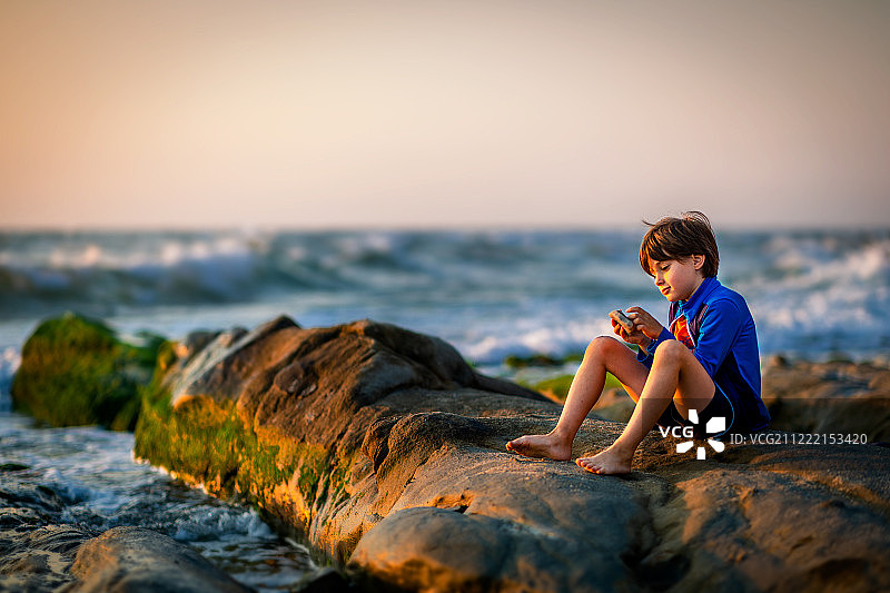 男孩在一个多石的海岸上玩耍，遇到了日出图片素材