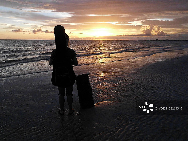 日出时沙滩上背着包的人的剪影图片素材