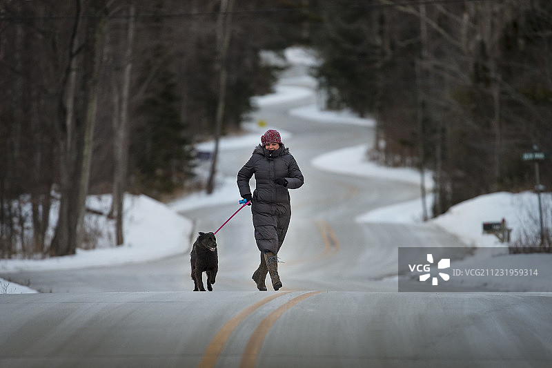 正视成熟的女人走在路上的狗在森林里的冬天图片素材