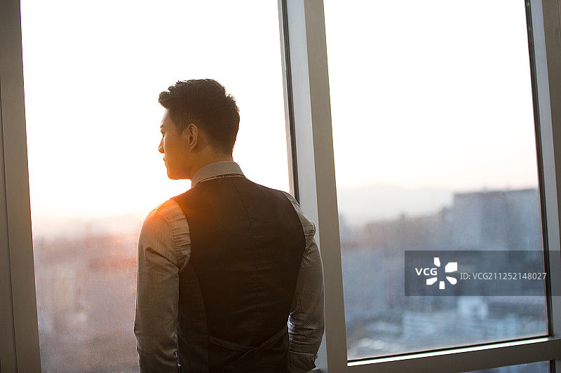 一个成功男商务人士站在办公大厦玻璃窗前思考工作看风景图片素材