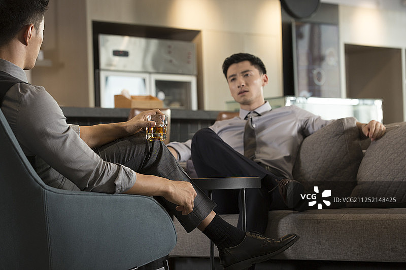 两个商务青年男子在酒店休闲区喝酒聊工作图片素材