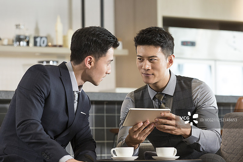 两个成功商务青年男子在酒店咖啡馆喝咖啡使用平板电脑沟通工作图片素材