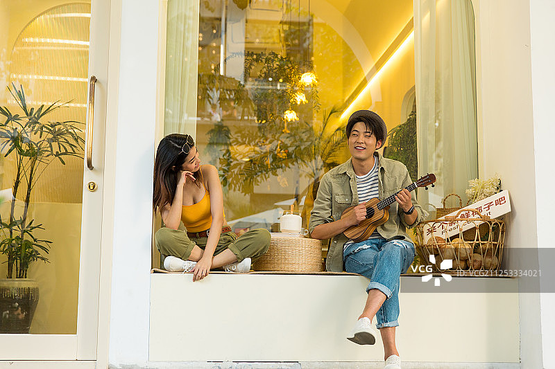 幸福情侣坐在户外甜品店飘窗上弹奏尤克里里琴吃椰子甜品嬉戏图片素材