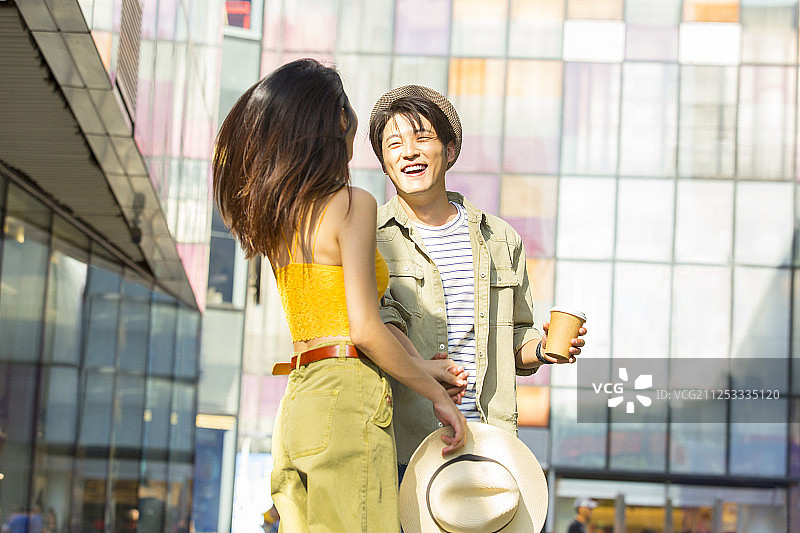 青年情侣在户外商业街手牵手拿着咖啡杯逛街旅行图片素材