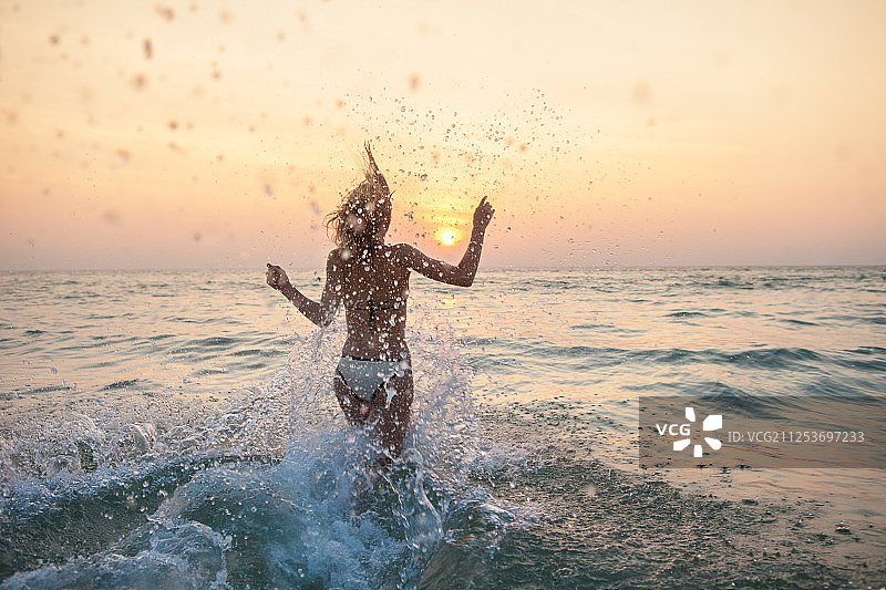 日落时分，女人在水里戏水图片素材