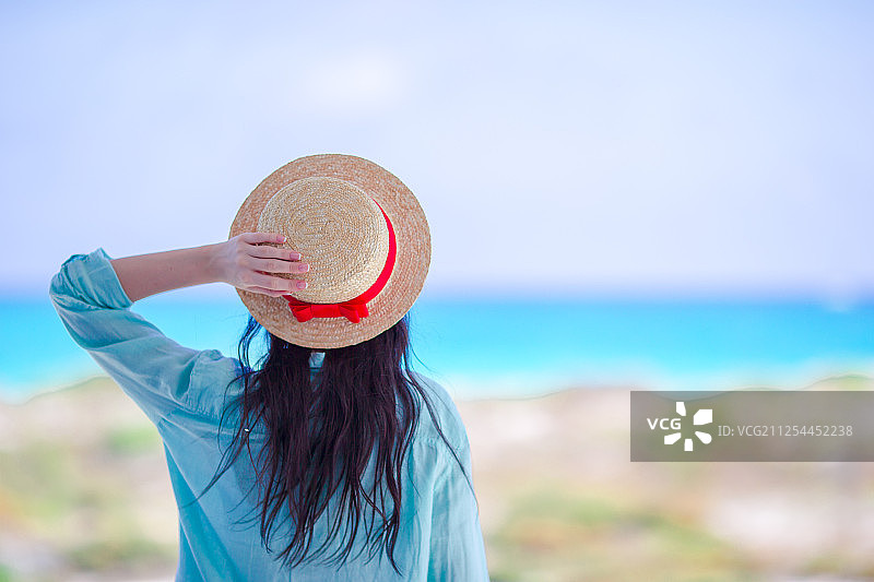 戴着帽子的年轻女子在热带海滩上看着美丽的大海图片素材