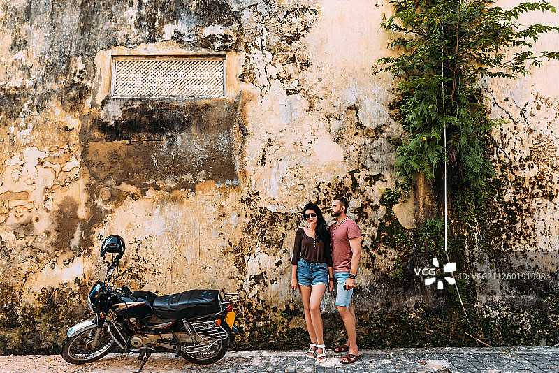 这对夫妇在斯里兰卡乘坐小型摩托车旅行。男人和女人在旅行。这对夫妇去亚洲旅行。骑摩托车独立旅行。男男女女在老墙上图片素材
