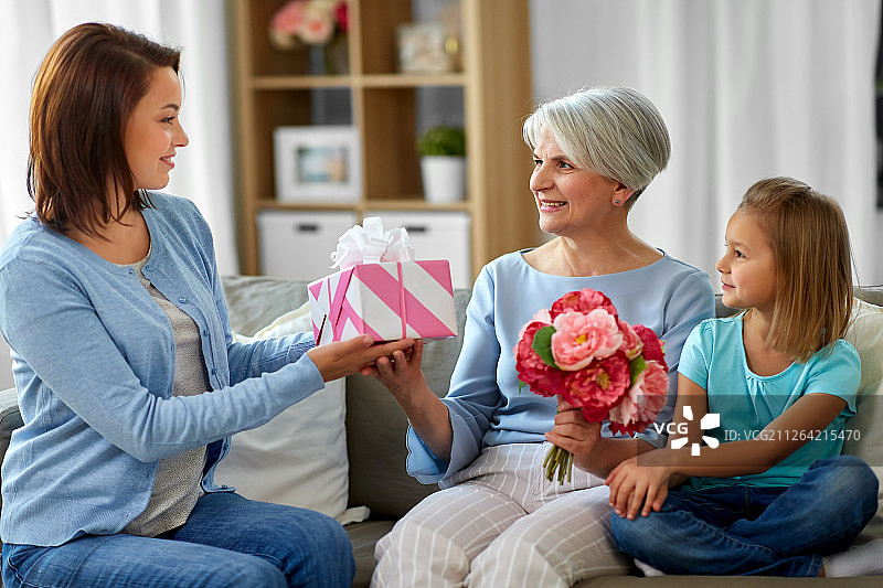 家庭，世代和生日快乐，母亲和女儿在家里给祖母送花和礼物。女性家庭赠送礼物给祖母图片素材