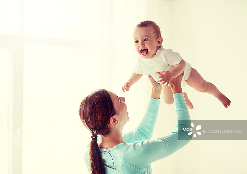 家庭，孩子和父母的概念-快乐的微笑年轻母亲和小婴儿在家里。快乐的年轻母亲和小婴儿在家图片素材