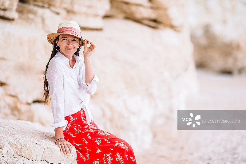 戴着帽子的女人坐在沙滩上的岩石上，对着镜头微笑图片素材