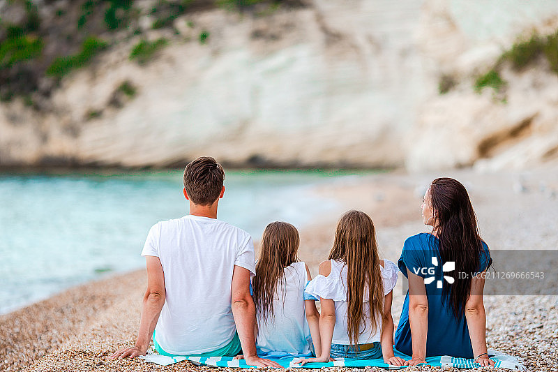 后视图的四家人坐在毛巾上的海滩在夏天图片素材