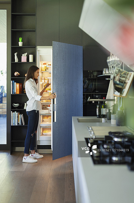 一个女人站在厨房打开的冰箱前图片素材