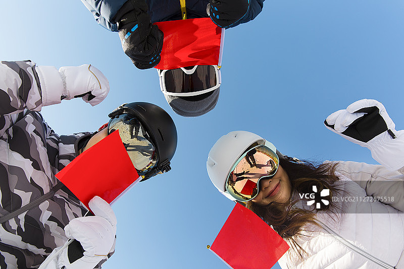 三个年轻男女拿着红旗在滑雪场为冬奥会加油喝彩图片素材