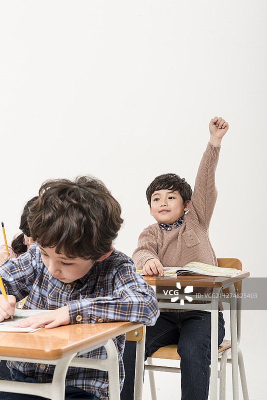 一群孩子坐在课桌旁举手的照片图片素材