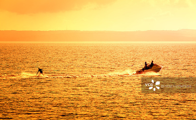 夏天日落金色海面上摩托艇和滑水运动员剪影图片素材