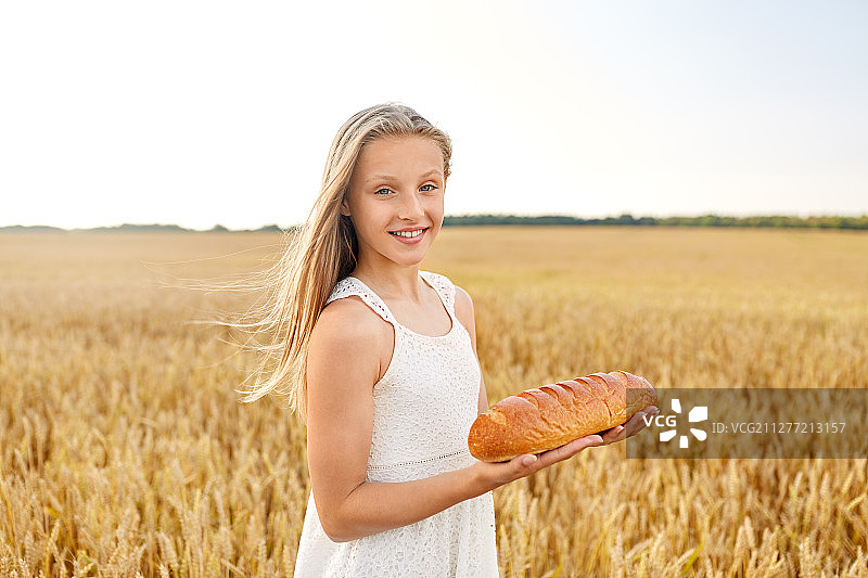 自然，健康的饮食和收获的概念-微笑的年轻女孩拿着一条白面包在谷物田在夏天。在谷物地里拿着白面包的女孩图片素材
