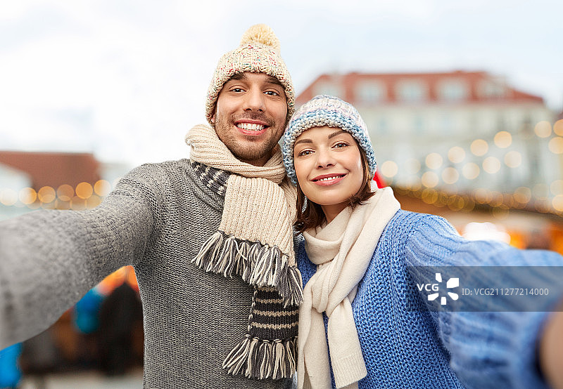 人们和冬季假期概念-幸福的夫妇在塔林老城的圣诞市场上编织帽子和围巾自拍。一对快乐的情侣在圣诞市场自拍图片素材