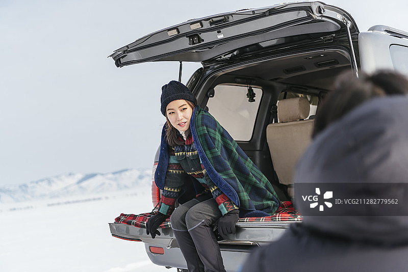 一名男子在雪地里拍摄一名女子坐在汽车后备箱上的照片图片素材