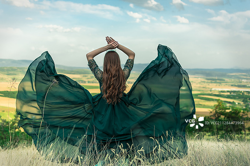 后视图的妇女在绿色连衣裙看农村景观，马里诺，马其顿图片素材