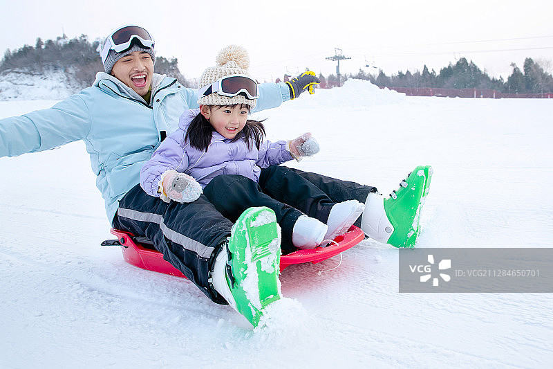 滑雪场上快乐父女坐着雪上滑板滑雪图片素材