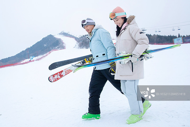青年伴侣手牵手拿着雪具在滑雪场行走图片素材