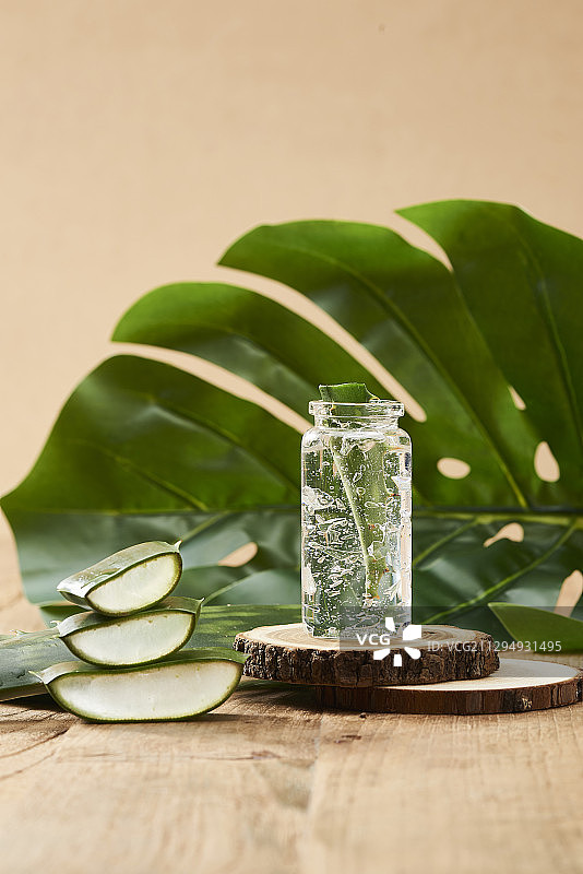 芦荟胶与芦荟片装于玻璃瓶内，芦荟片与树叶装饰放在木地板上图片素材