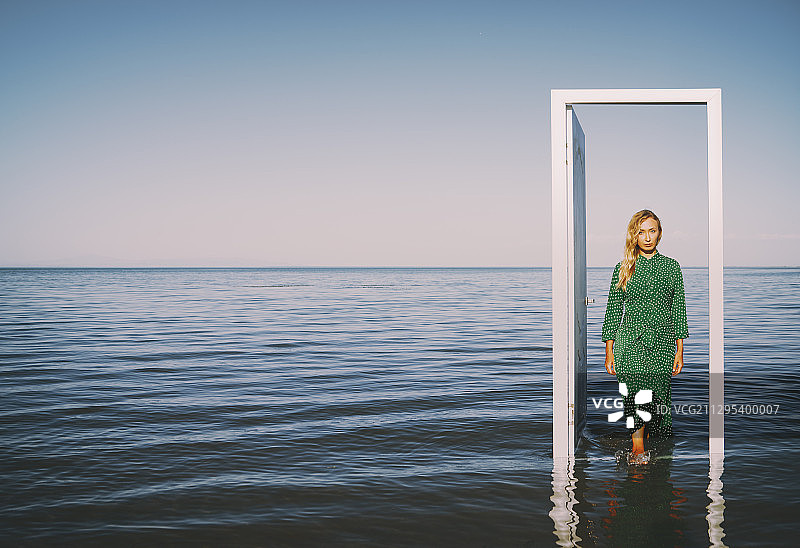 美丽的女人站在海边，就在门口。超现实的上下文。非常适合书的封面图片素材