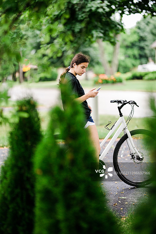 年轻女子在车道上骑自行车时使用手机图片素材