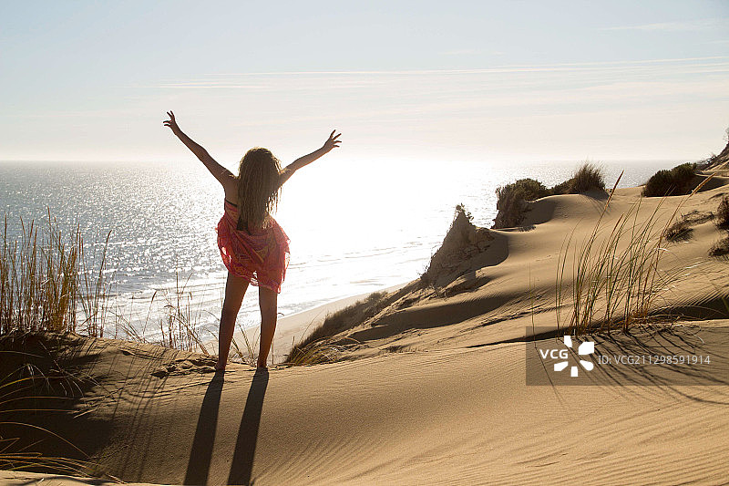 在海边沙丘上挥舞着手臂的年轻女子，韦尔瓦，西班牙图片素材