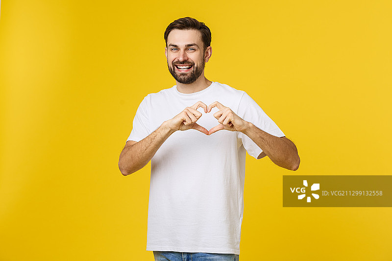 微笑的男人做心脏的手势在他的胸部与白衬衫孤立在黄色的背景图片素材