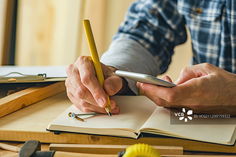 塞尔维亚诺维萨德，木匠在桌子上使用手机和在笔记本上写作的中间部分图片素材