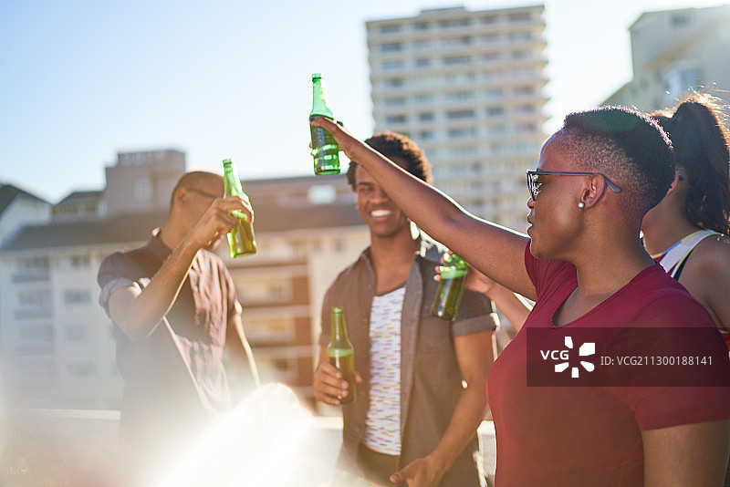 无忧无虑的年轻朋友在阳光明媚的城市阳台上喝啤酒图片素材