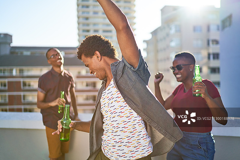 无忧无虑的年轻朋友们在阳光灿烂的屋顶上跳舞喝啤酒图片素材