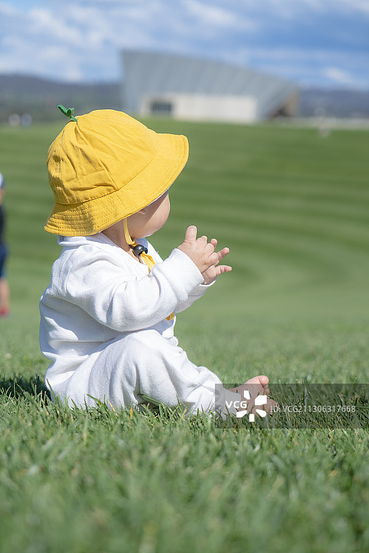 坐在山坡草坪上开心拍手的小黄帽婴儿图片素材