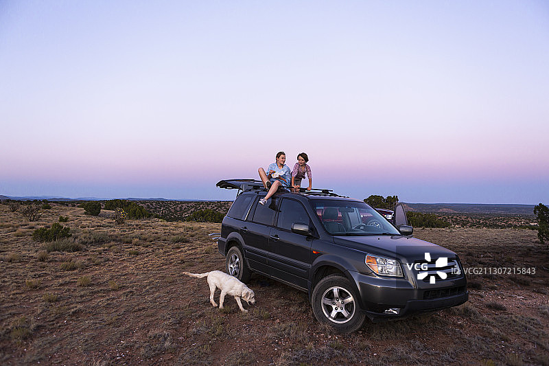 日落时分，一个十几岁的女孩和她的弟弟坐在他们的SUV上。图片素材