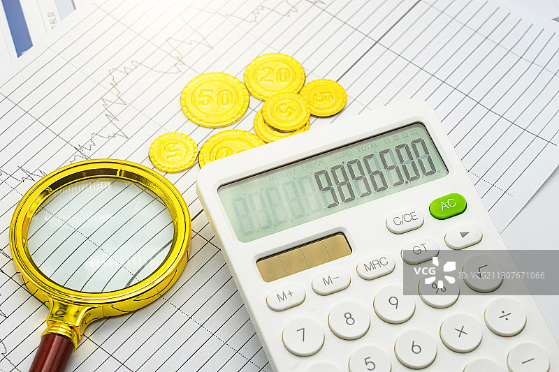 金融经济图表上的计算器、放大镜和硬币图片素材