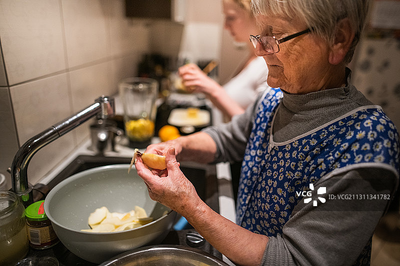 波兰，一位年长的女士在和孙女一起烤蛋糕时切苹果图片素材
