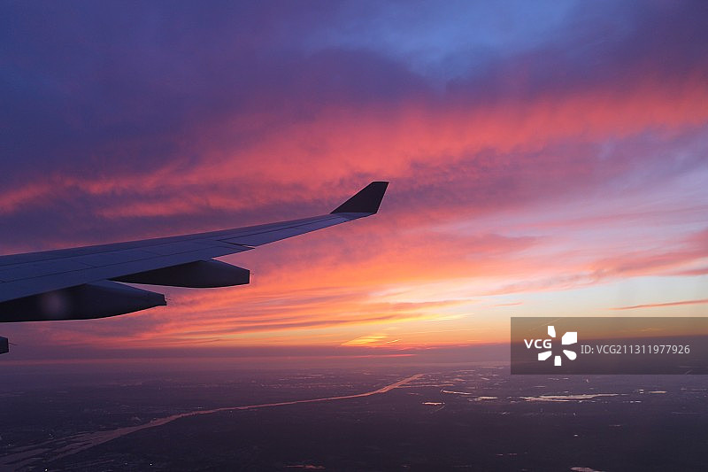 裁剪图像的飞机机翼在日落时对着天空飞行图片素材