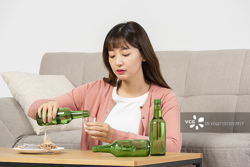 女人坐在桌边喝着烧酒，在沙发前吃着小吃，看起来很担心图片素材
