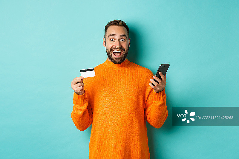 一个微笑的男人拿着信用卡，站在蓝色的背景下图片素材
